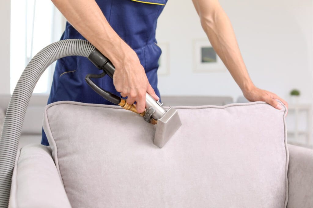 a person cleaning sofa back seat with vacuum cleaner.