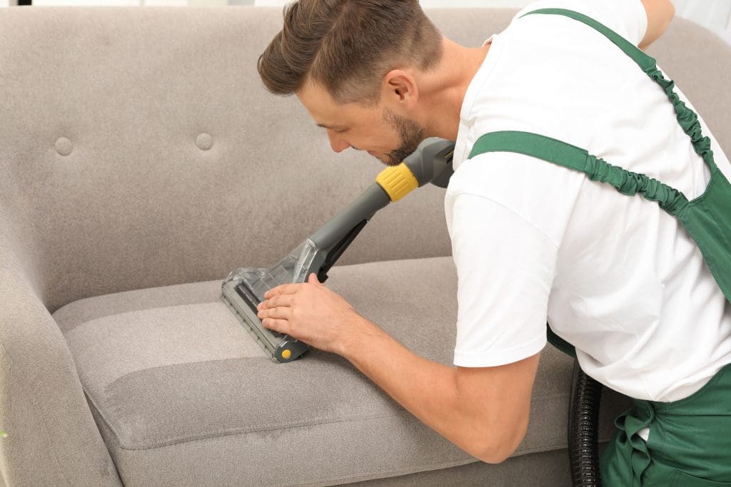 a person cleaning sofa with vacuum cleaner.