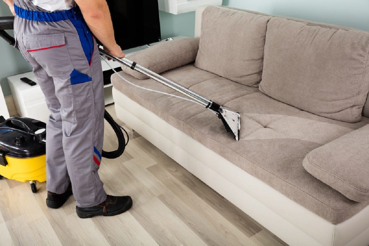 a person cleaning sofa with vacuum cleaner, sofa color is grey {{brizy_dc_image_alt entityId=